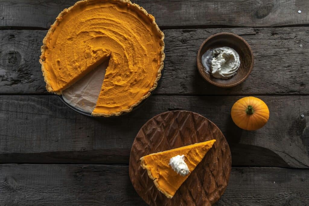 Saftiger Pumpkin Spice Kuchen mit echtem Kürbis auf rustikalem Holztisch, dekoriert mit Schlagsahne – natürliches Herbstrezept für longevity und slow aging Ernährung.
