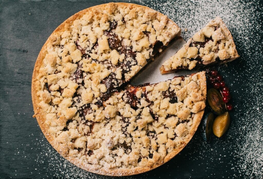 Anschnitt eines Pflaumenkuchens mit Zimt und Streuseln – inspiriert vom Duftprofil der AVA & MAY PLUM CAKE Duftkerze mit fruchtig-süßer Note.