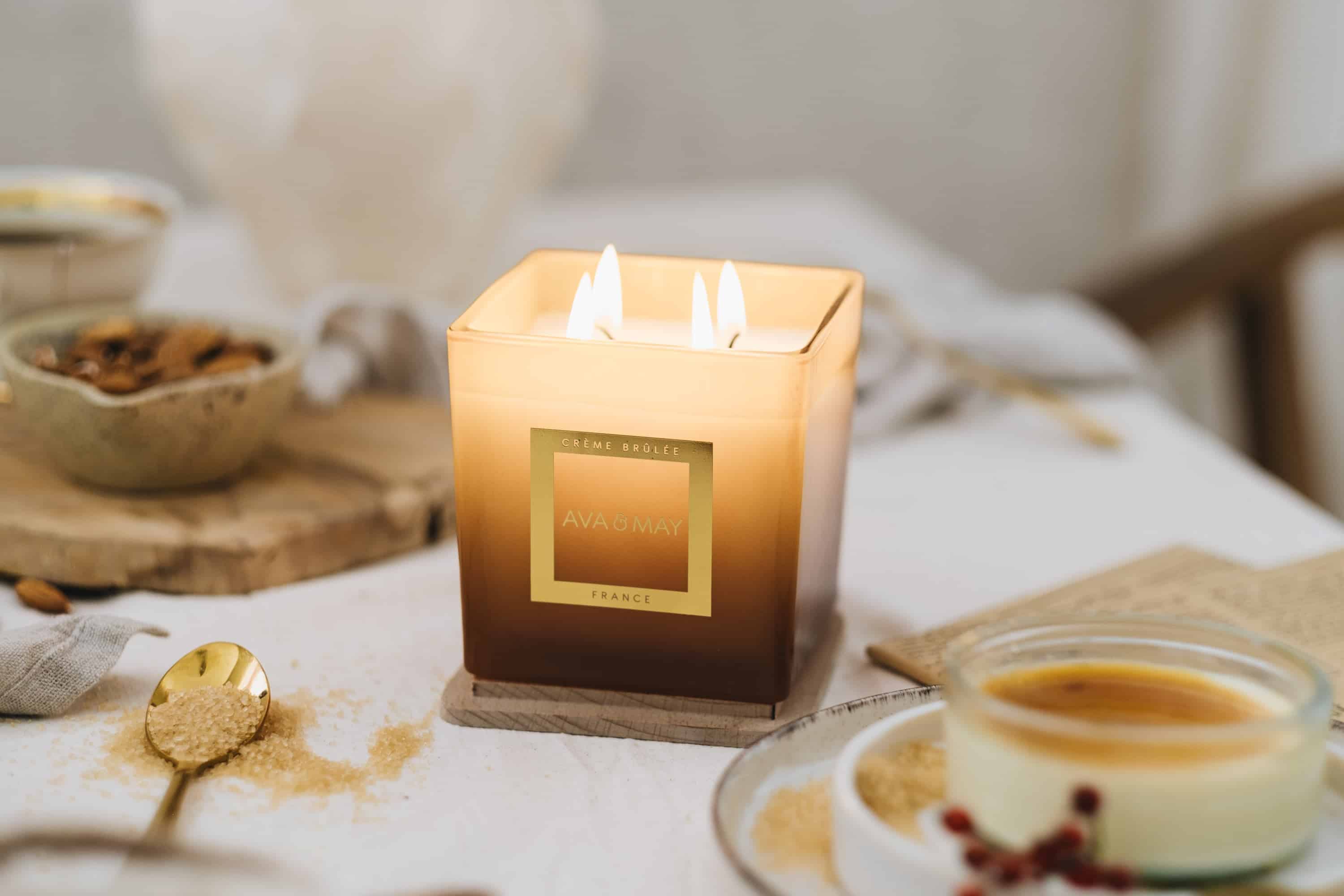 AVA & MAY CRÈME BRÛLÉE Duftkerze im goldbraunen eckigen Glas mit vier Flammen, umgeben von Zucker, Vanille und Dessert-Inspirationen.