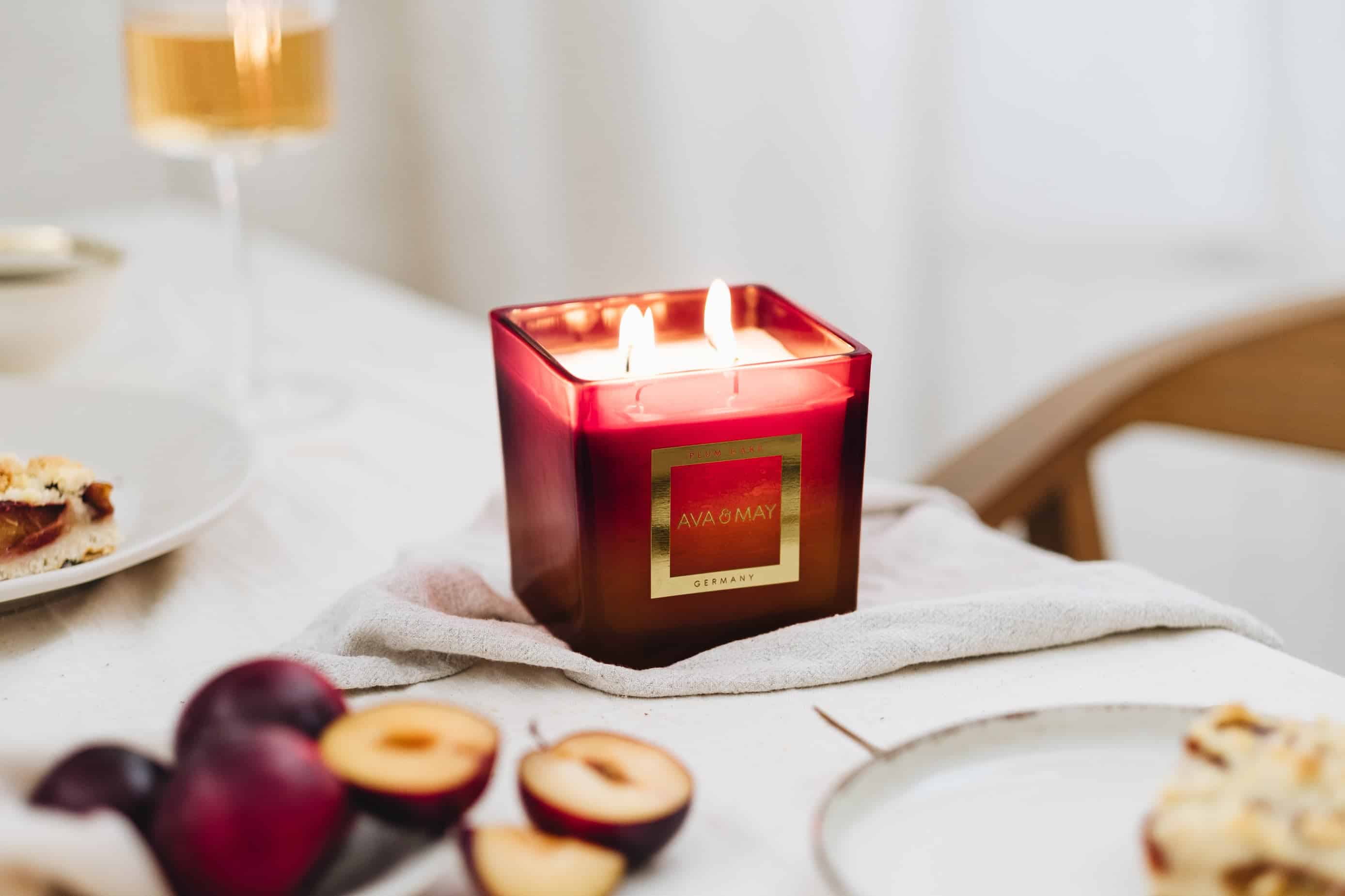 AVA & MAY PLUM CAKE Duftkerze im roten eckigen Glas mit zwei Flammen, dekoriert mit frischen Pflaumen und Kuchenstücken.